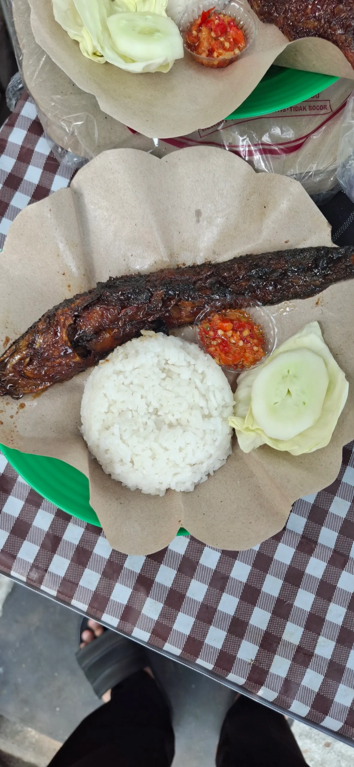Lele bakar dengan nasi, sambal, timun, dan kol di atas kertas nasi.